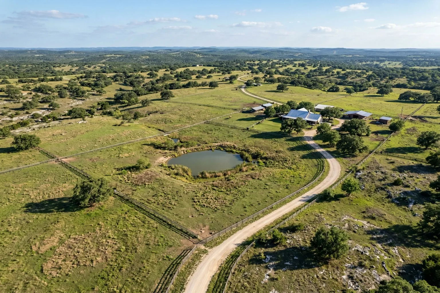 Aerial view of a Texas Hill Country ranch with cross-fenced pastures, stock tank, and live oak trees
