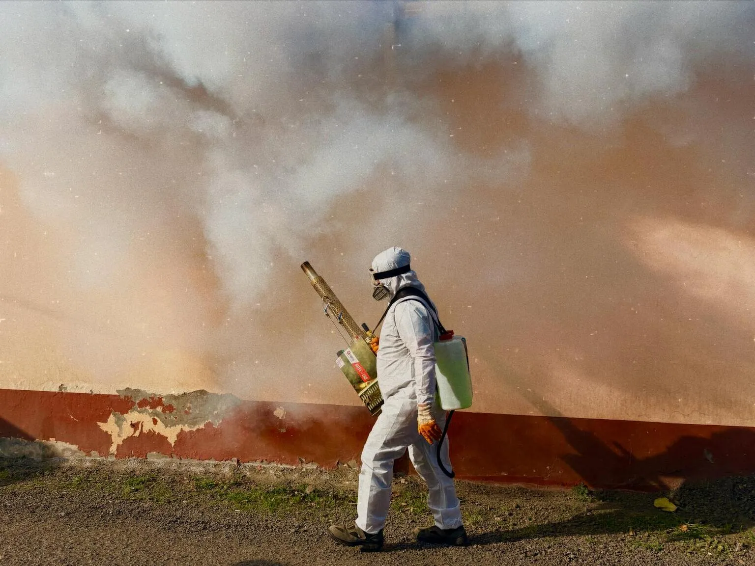 Professional pest control technician spraying treatment around home exterior