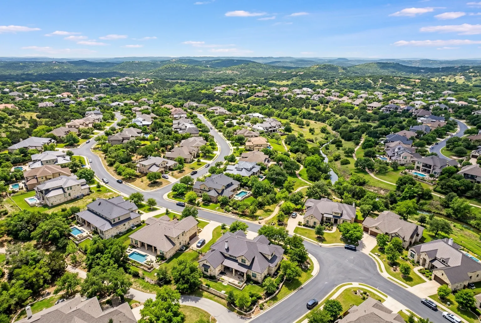 Aerial view of residential homes in the Texas Hill Country west of Austin with rolling green hills