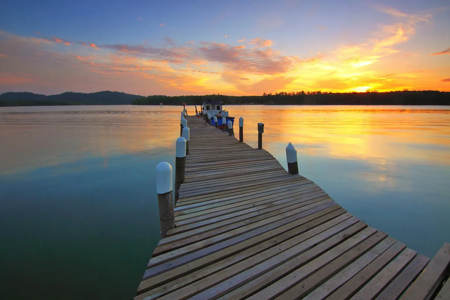 Wooden dock at sunset with boats moored at a marina on calm lake water