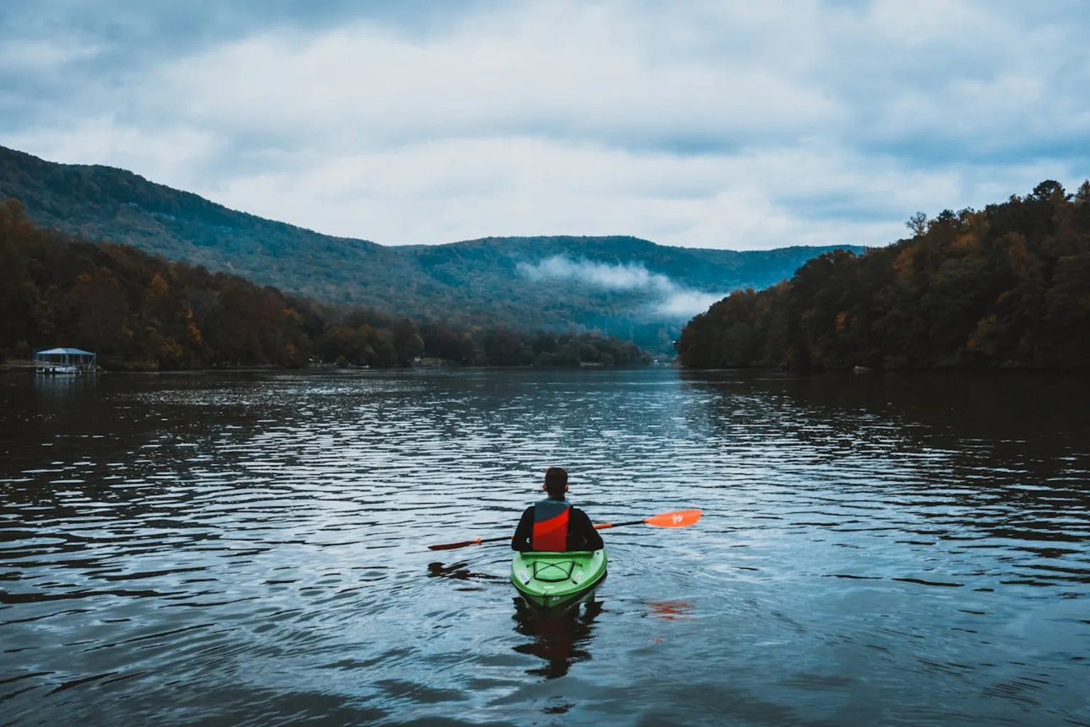 Kayaker on calm lake with scenic mountain backdrop and misty conditions