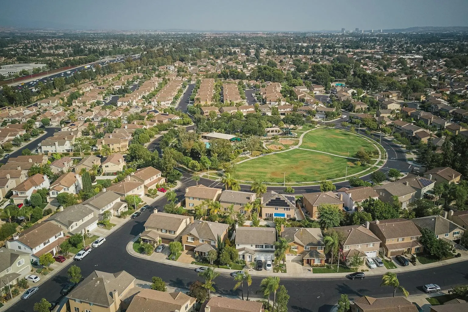Drone view of suburban neighborhood showing central green space and varied residential lots