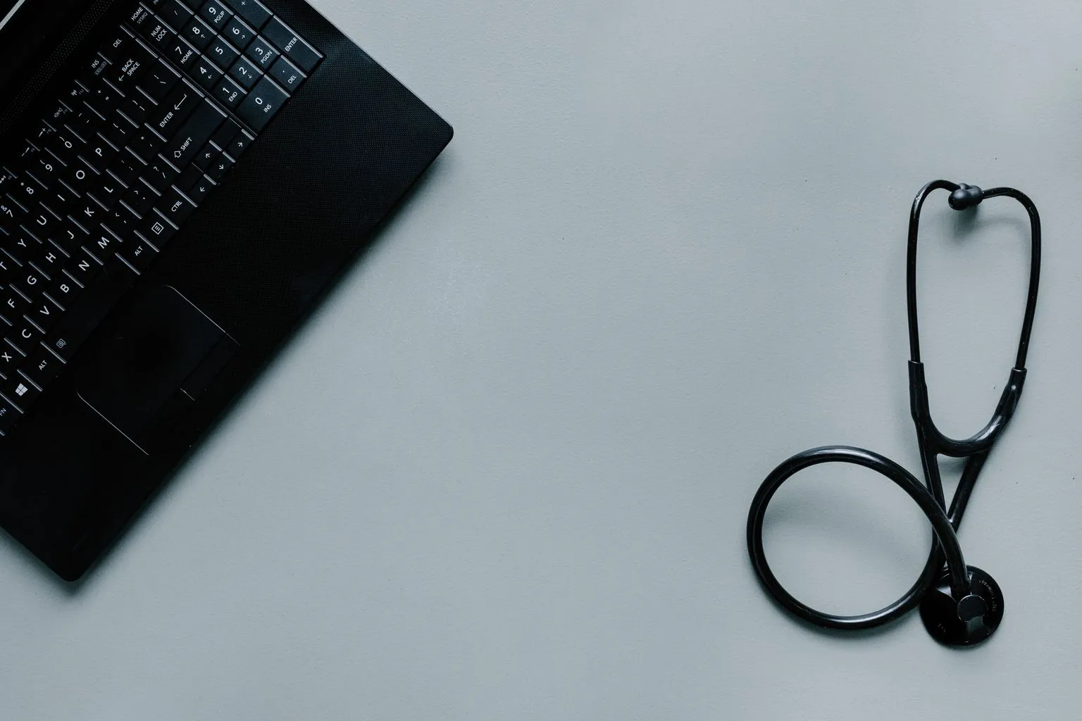 Laptop computer and stethoscope on dark surface representing telehealth services