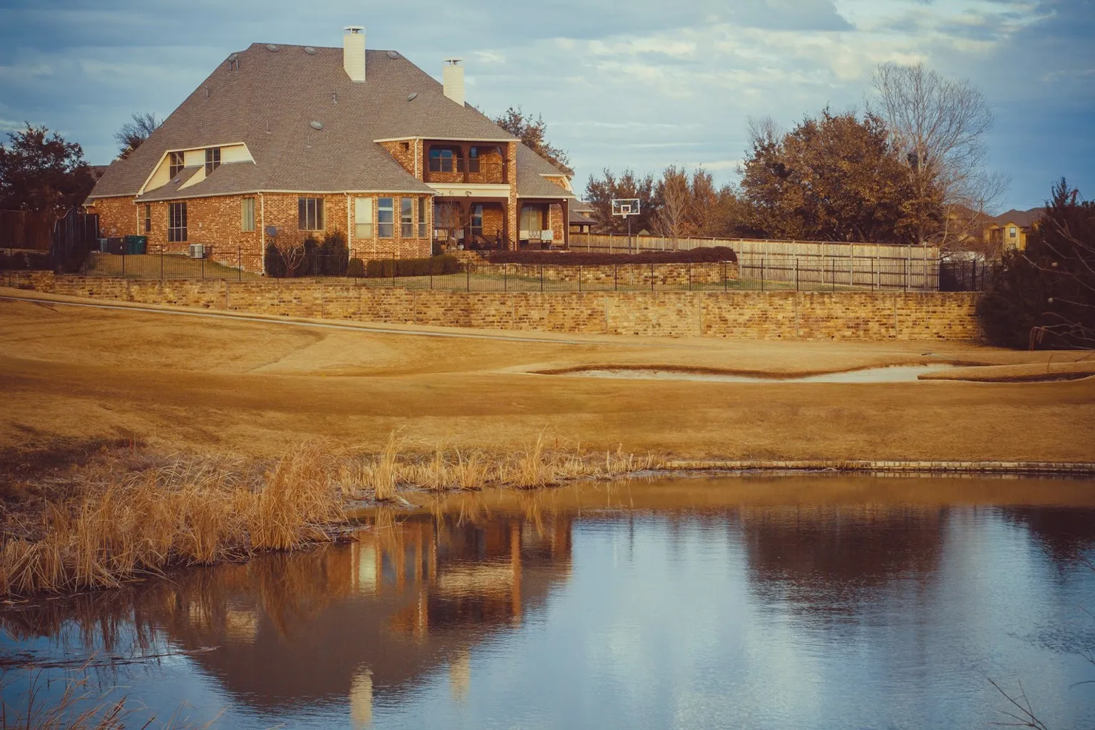 Two-story brick Texas home beside a neighborhood pond at golden hour