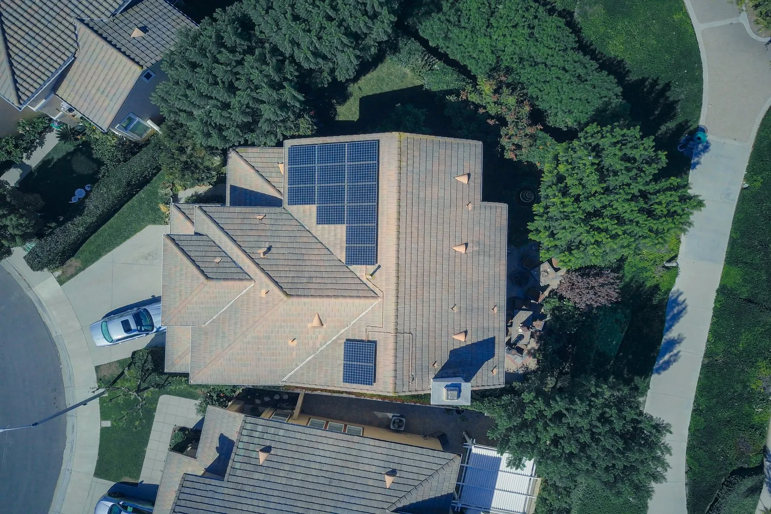 Aerial view of a residential home with solar panels installed on the roof surrounded by trees and landscaping